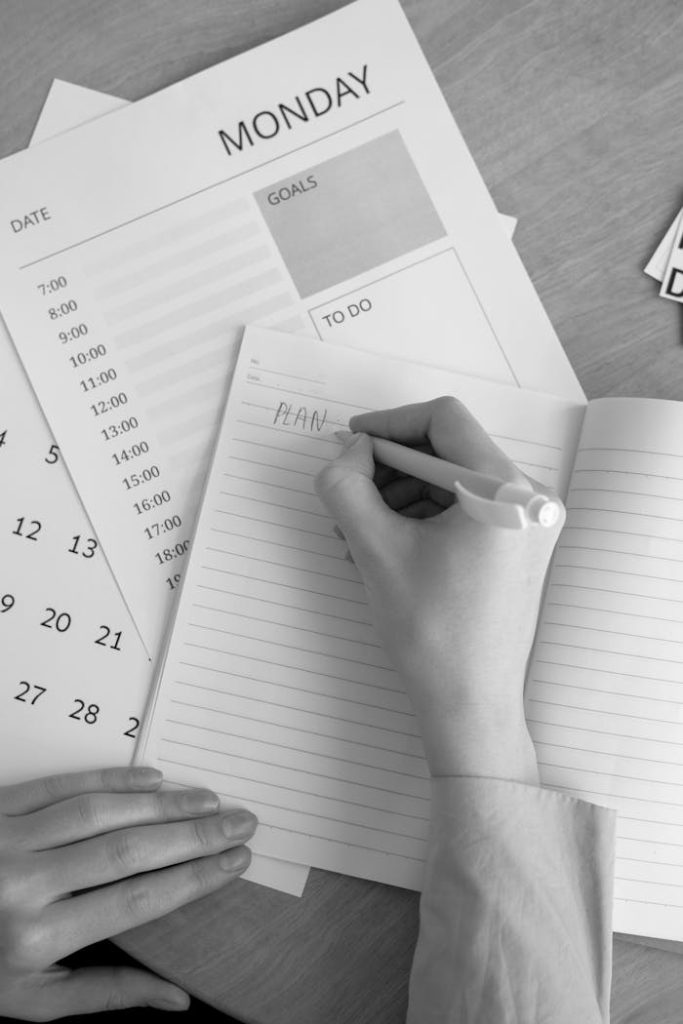 hand-writing-on-notepad-7550886 A monochrome image of a person planning their week with a notebook, calendar, and goals list.